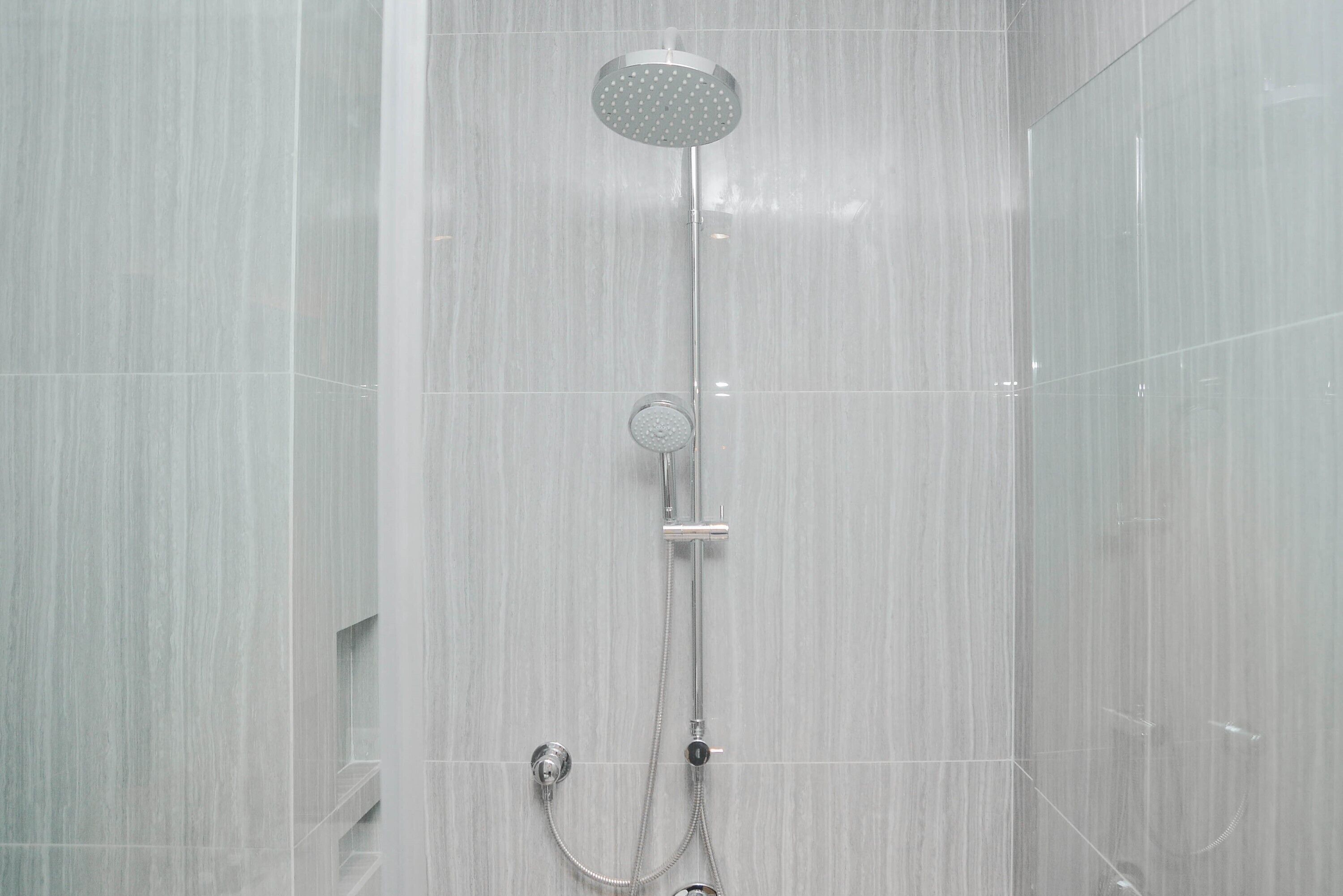 A modern shower with a rain showerhead and handheld showerhead, mounted on a wall with a vertical drain.