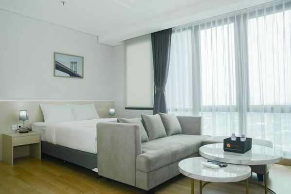 A modern hotel room with a bed, a sofa, a small table, and a window with curtains.
