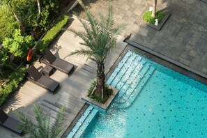 An aerial view of a swimming pool with a wooden deck, lounge chairs, and a palm tree. - New Furnished 2BR Apartment at Capitol Park Residence (Jakarta)