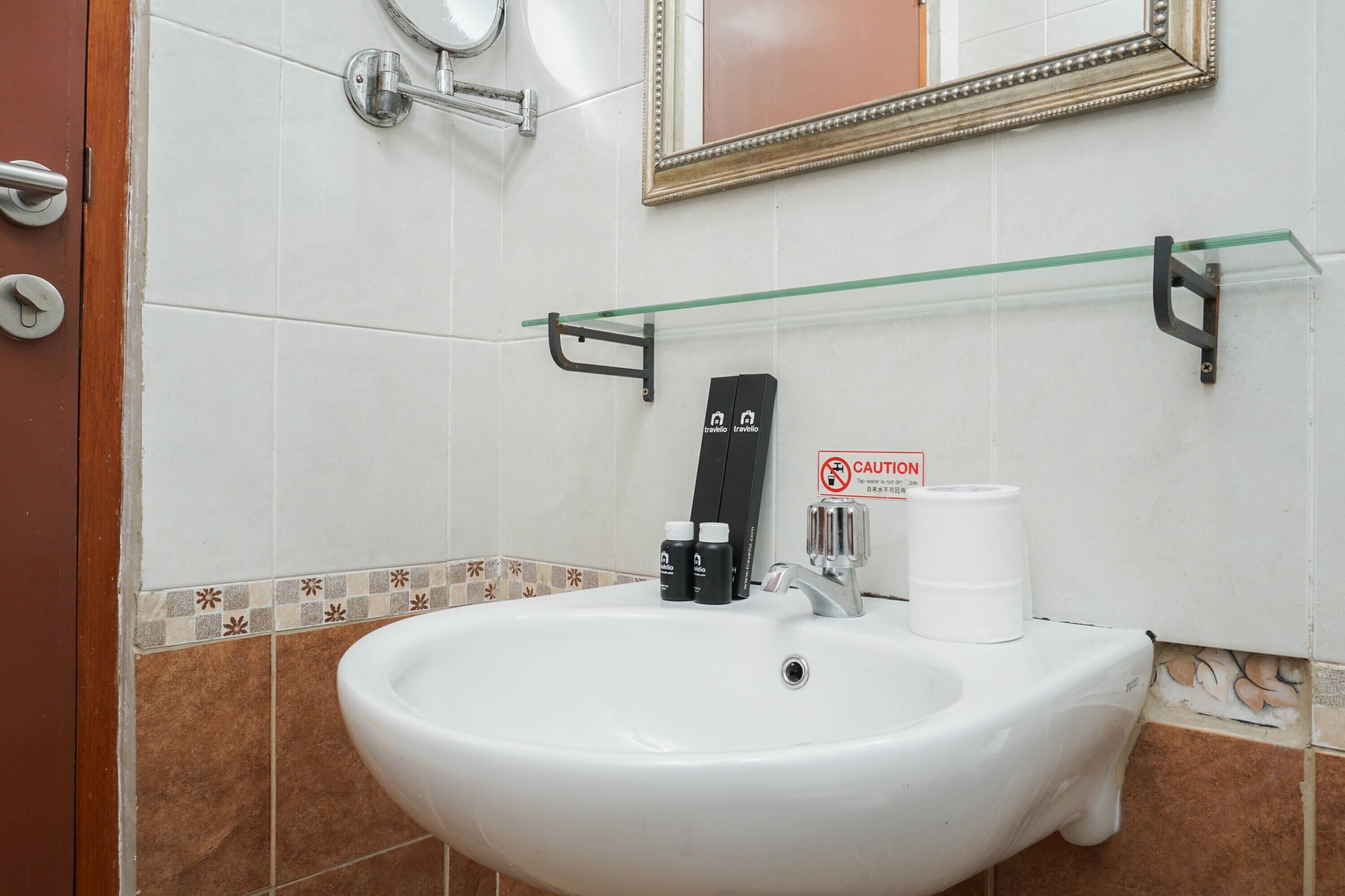 A bathroom with a white sink, a mirror, a framed mirror above, and a caution sign on the wall.