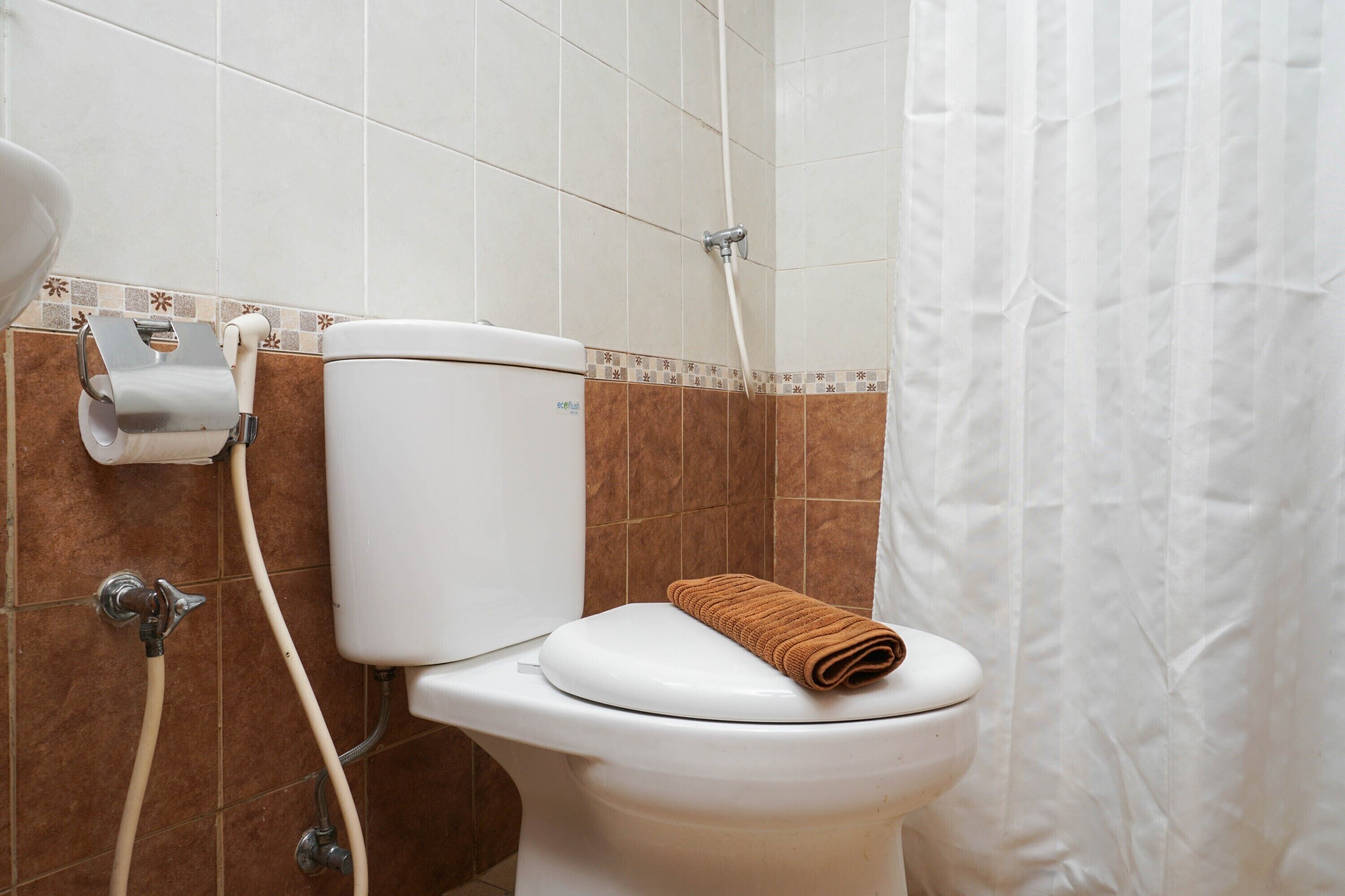 A bathroom with a toilet, a paper towel dispenser, and a shower curtain.