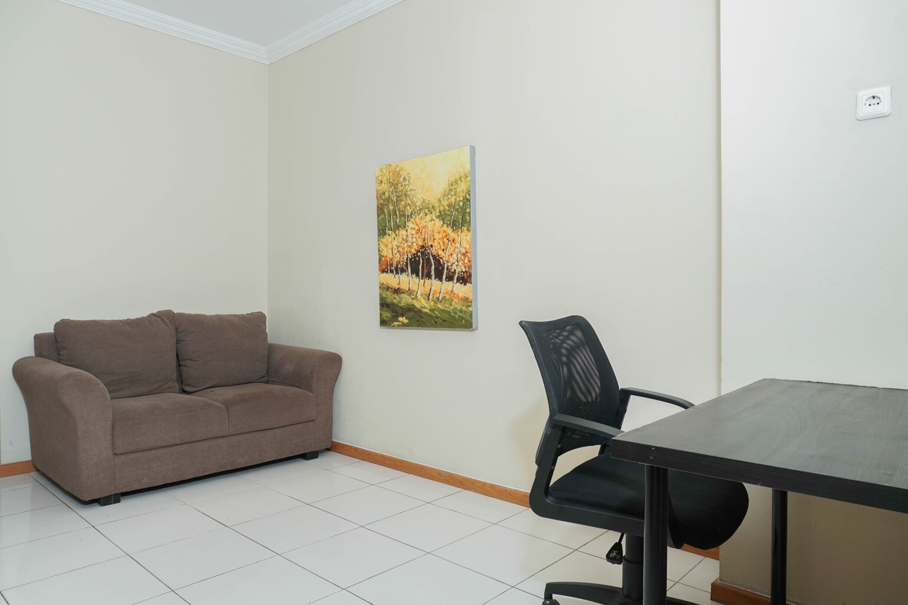 A room with a brown sofa, a black office chair, and a table.