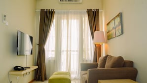 A hotel room with a TV, a sofa, a small table, a lamp, and a painting on the wall. - 3BR Business Residence at Grand Palace Kemayoran (Jakarta)