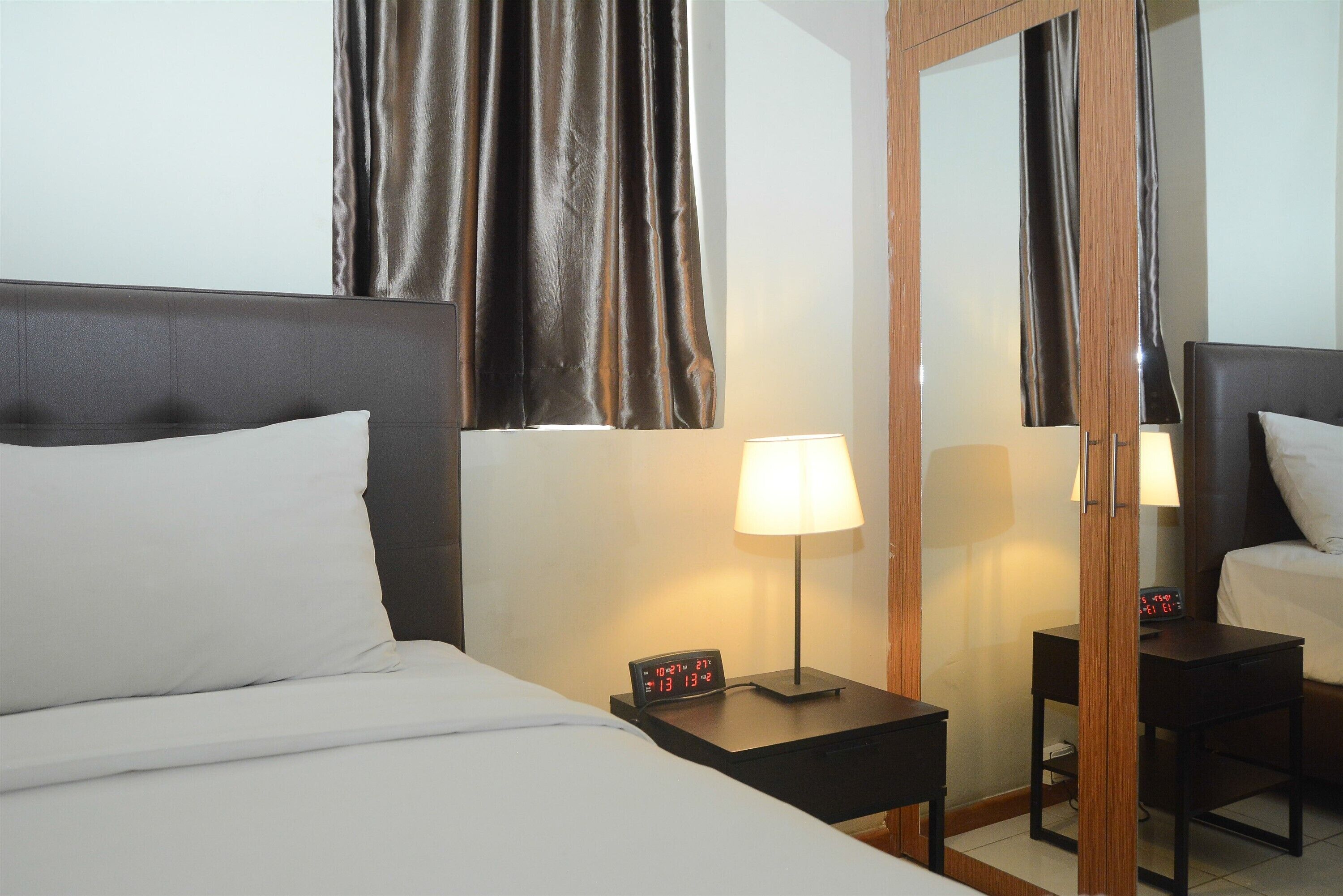 A hotel room with a bed, a nightstand with a lamp, a digital clock, and a mirror.