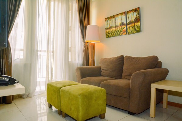 A living room with a brown sofa, a yellow ottoman, a lamp, and a painting on the wall.