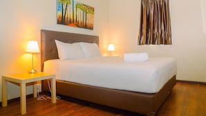 A neatly made bed with white linens, a wooden nightstand with a lamp, and a painting of trees on the wall. - 3BR Business Residence at Grand Palace Kemayoran (Jakarta)