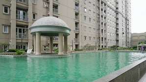 A swimming pool with a gazebo in the center, surrounded by a high-rise building with balconies. - 3BR Business Residence at Grand Palace Kemayoran (Jakarta)