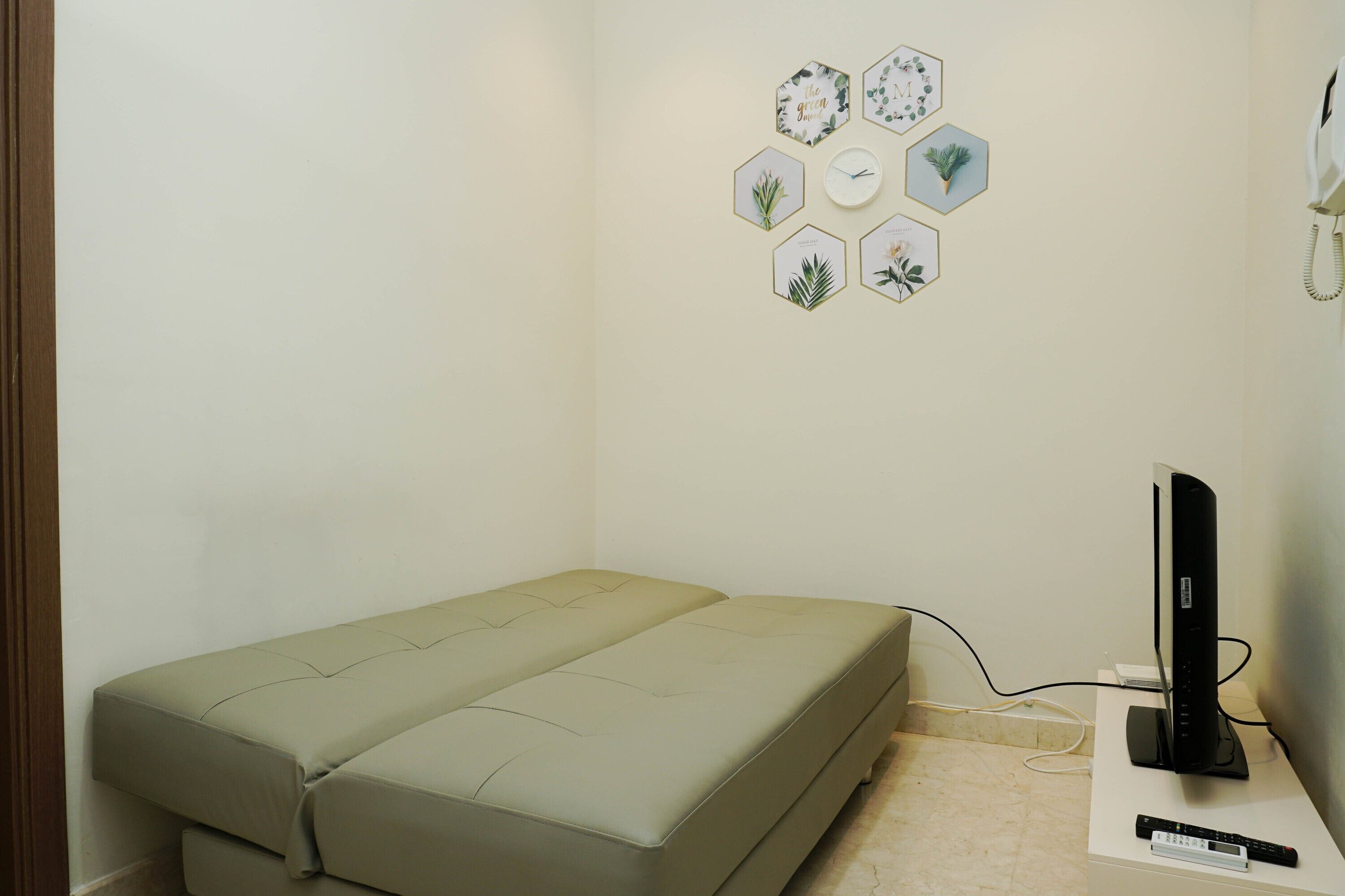 Une petite pièce comprenant un lit, un téléviseur et un mur décoré d’œuvres d’art aux motifs hexagonaux.