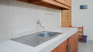 A kitchen with a stainless steel sink, white tiled backsplash, wooden cabinets, and a metal towel rack. - Elegant and Homey 2BR Hampton's Park Apartment (Jakarta)