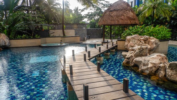 A swimming pool with a wooden deck and a thatched-roof structure. - Elegant and Homey 2BR Hampton's Park Apartment (Jakarta)