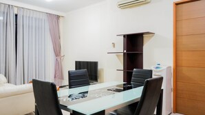 A modern living room with a glass-top dining table, black chairs, a white sofa, a wooden cabinet, and a white radiator. - Elegant and Homey 2BR Hampton's Park Apartment (Jakarta)