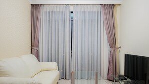 A living room with a sofa, a glass coffee table, a flat-screen TV, and a sliding glass door with curtains. - Elegant and Homey 2BR Hampton's Park Apartment (Jakarta)