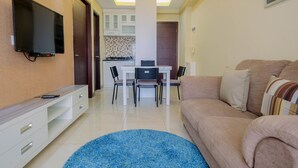 Una sala moderna con una televisión de pantalla plana, un sofá, una mesa de centro y un comedor con una mesa y sillas.