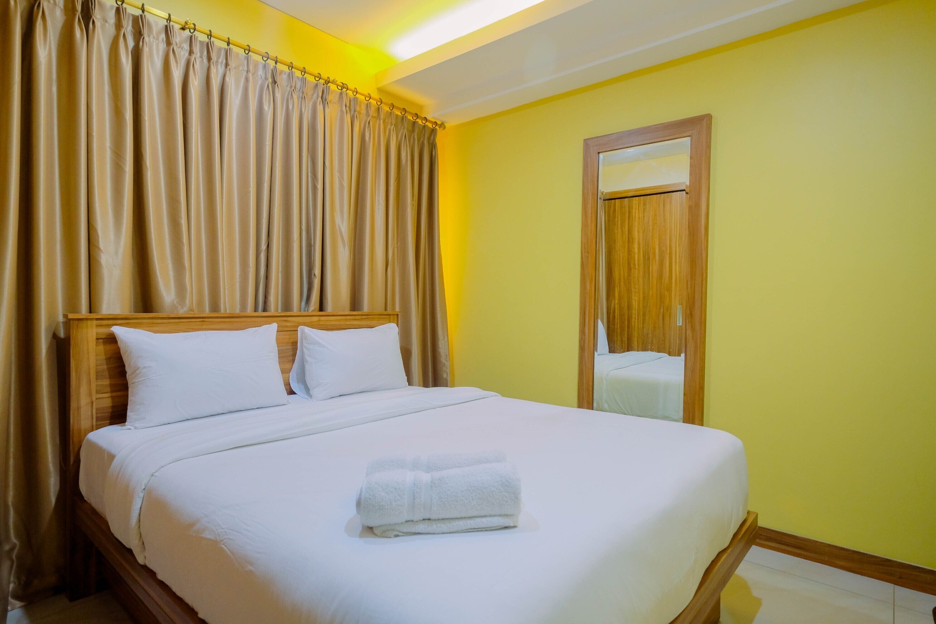 A neatly made bed with white linens and a folded towel, a wooden headboard, and a mirror on the wall.