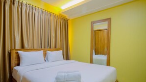 Una cama bien hecha con sábanas blancas y una toalla doblada, un cabecero de madera y un espejo en la pared.