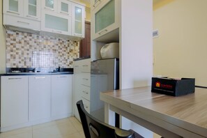 Une cuisine de taille réduite avec des meubles blancs, un dosseret à carreaux et un réfrigérateur. Une boîte noire portant l’inscription « Travelio » est posée sur le comptoir.