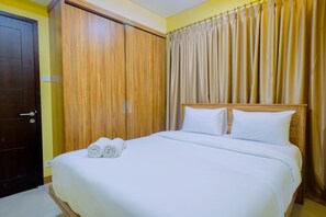 Un lit bien fait, avec du linge de lit blanc et des serviettes pliées, une armoire en bois et une fenêtre recouverte d’un rideau.