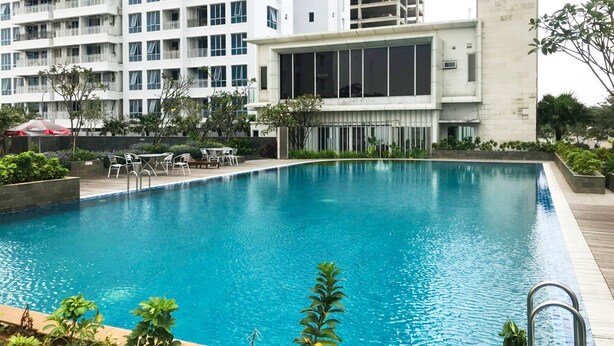 Una piscina con cubierta de madera, rodeada de vegetación y un edificio moderno con amplios ventanales.