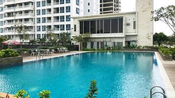 A swimming pool with a wooden deck, surrounded by greenery and a modern building with large windows.