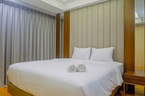 A neatly made bed with white linens and two rolled towels, a wooden headboard, and a large window with curtains.