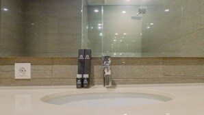 A modern bathroom with a large mirror, a glass shower enclosure, and toiletries on the counter.