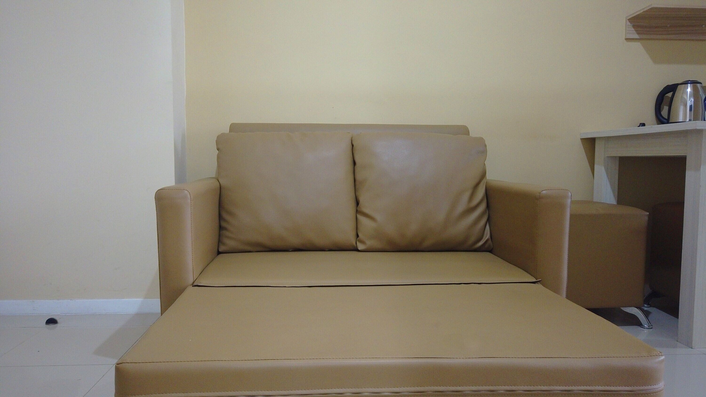 Un sofá color beige con un otoman a juego en una habitación con piso de baldosas y una pequeña mesa con una tetera.