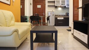 Ein Wohnzimmer mit einer Couch, einem Couchtisch und einer Küchenzeile mit Schränken und einem Kühlschrank.