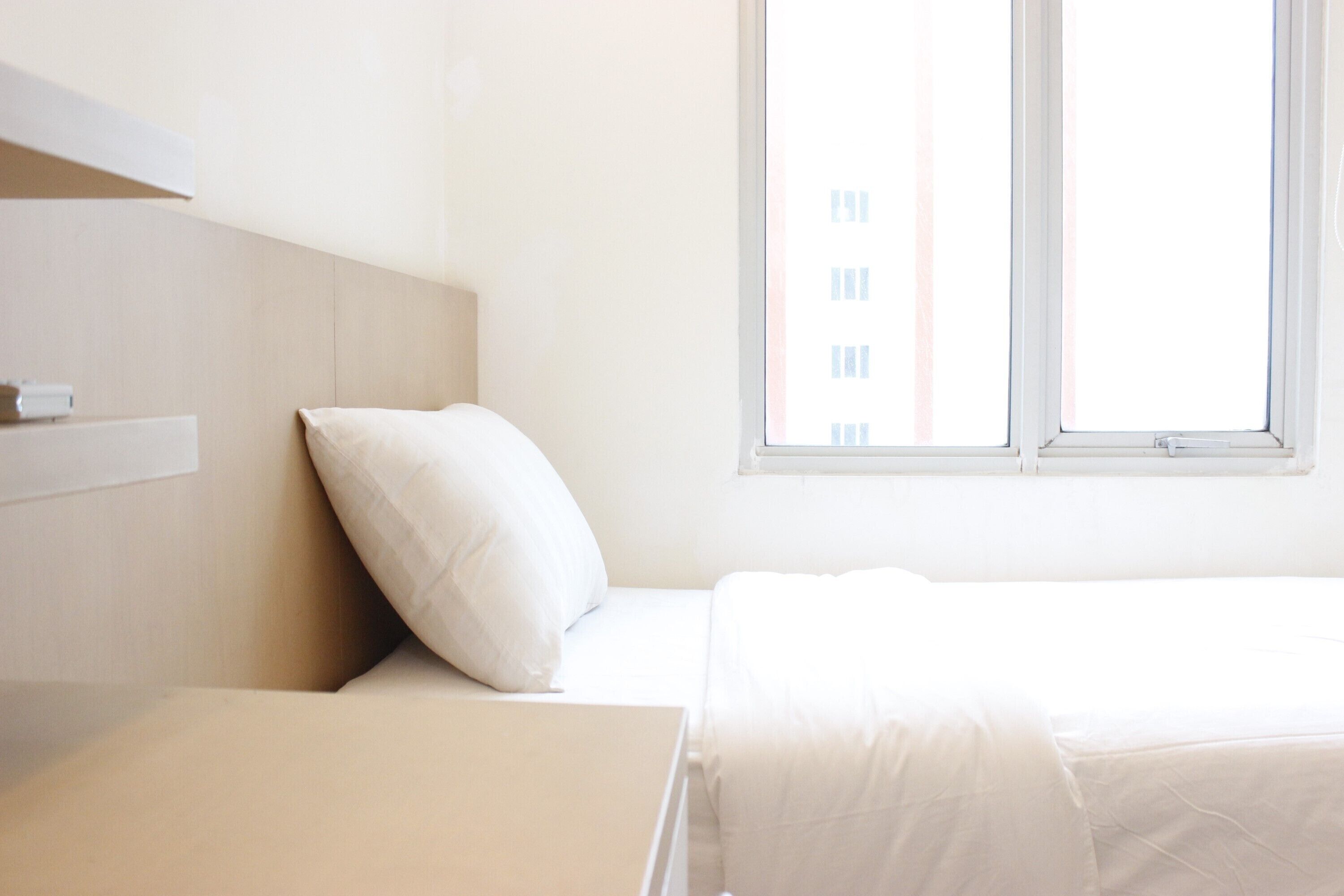 A minimalist hotel room with a bed, a nightstand, and a window with a view of buildings.