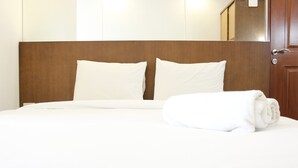 Ein ordentlich gemachtes Bett mit weißen Leinen und Kissen, ein Holz-Kopfteil und ein gefaltetes Handtuch daneben.