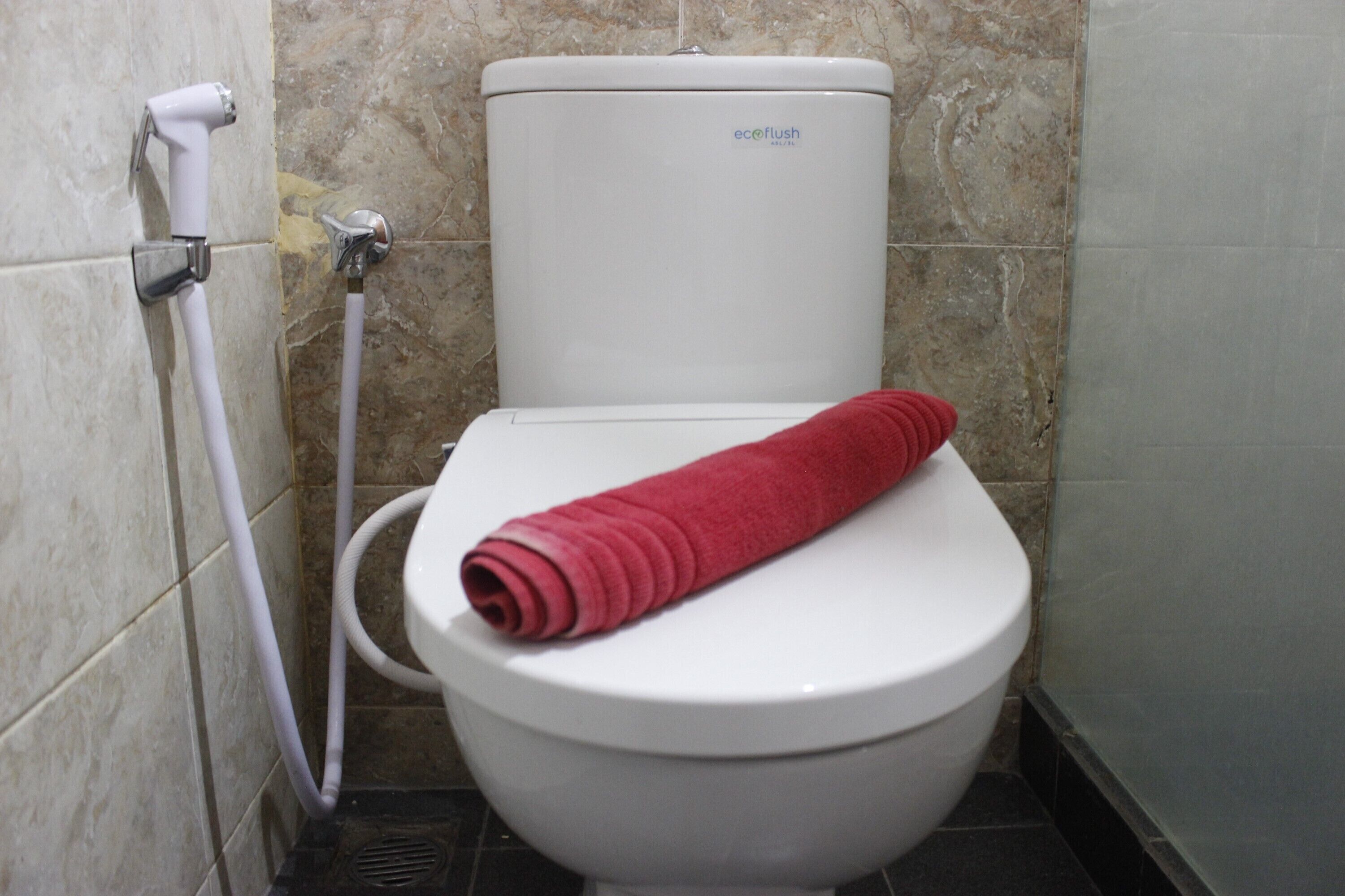 A white toilet with a red towel on the seat and a water pipe to the left.