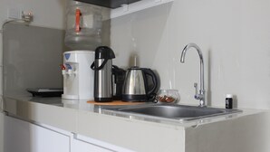 A kitchen with a water dispenser, coffee maker, kettle, and a sink. - Compact 2BR @ Galeri Ciumbuleuit 2 Apartment near Dago (Bandung)