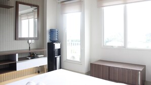 A hotel room with a bed, a desk, a mirror, a water dispenser, and a window with a view. - Affordable Studio Galeri Ciumbuleuit 2 Apartment near Dago (Bandung)