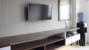 A modern living room with a flat-screen TV mounted on the wall, a large water dispenser, and a wooden entertainment unit with built-in shelves. - Affordable Studio Galeri Ciumbuleuit 2 Apartment near Dago (Bandung)
