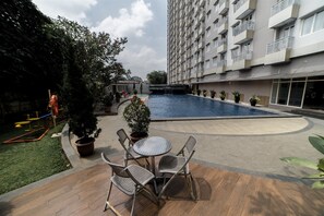 A courtyard with a swimming pool, outdoor seating, and a tall residential building. - Affordable Studio Galeri Ciumbuleuit 2 Apartment near Dago (Bandung)