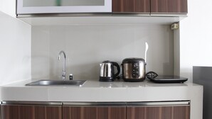 A kitchen with a stainless steel sink, a kettle, and a coffee maker on the countertop. - Affordable Studio Galeri Ciumbuleuit 2 Apartment near Dago (Bandung)