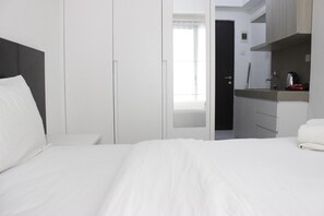 Habitación de hotel con cama, mesita de noche, armario y zona de kitchenette.