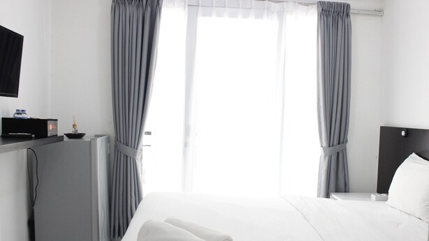 Una habitación de hotel moderna con una cama bien hecha, un escritorio con un ordenador y un televisor de pantalla plana montado en la pared.