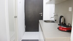 Cocina compacta con una puerta oscura, un lavamanos y un electrodoméstico rojo, probablemente una cafetera o tostadora.