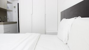 Ein modernes Schlafzimmer mit Bett, weißen Wänden und einem dunklen Kopfteil.