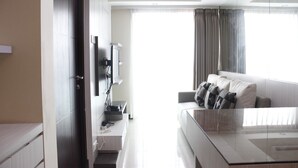 A modern hotel room with a glass coffee table, a sofa with cushions, a flat-screen TV, a desk with a computer, and a wardrobe. - Brand New 2BR @ Tamansari La Grande Apartment Bandung (Bandung)
