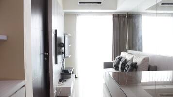 Una habitación de hotel moderna con una mesa de centro de vidrio, un sofá con cojines, un televisor de pantalla plana, un escritorio con ordenador y un armario.