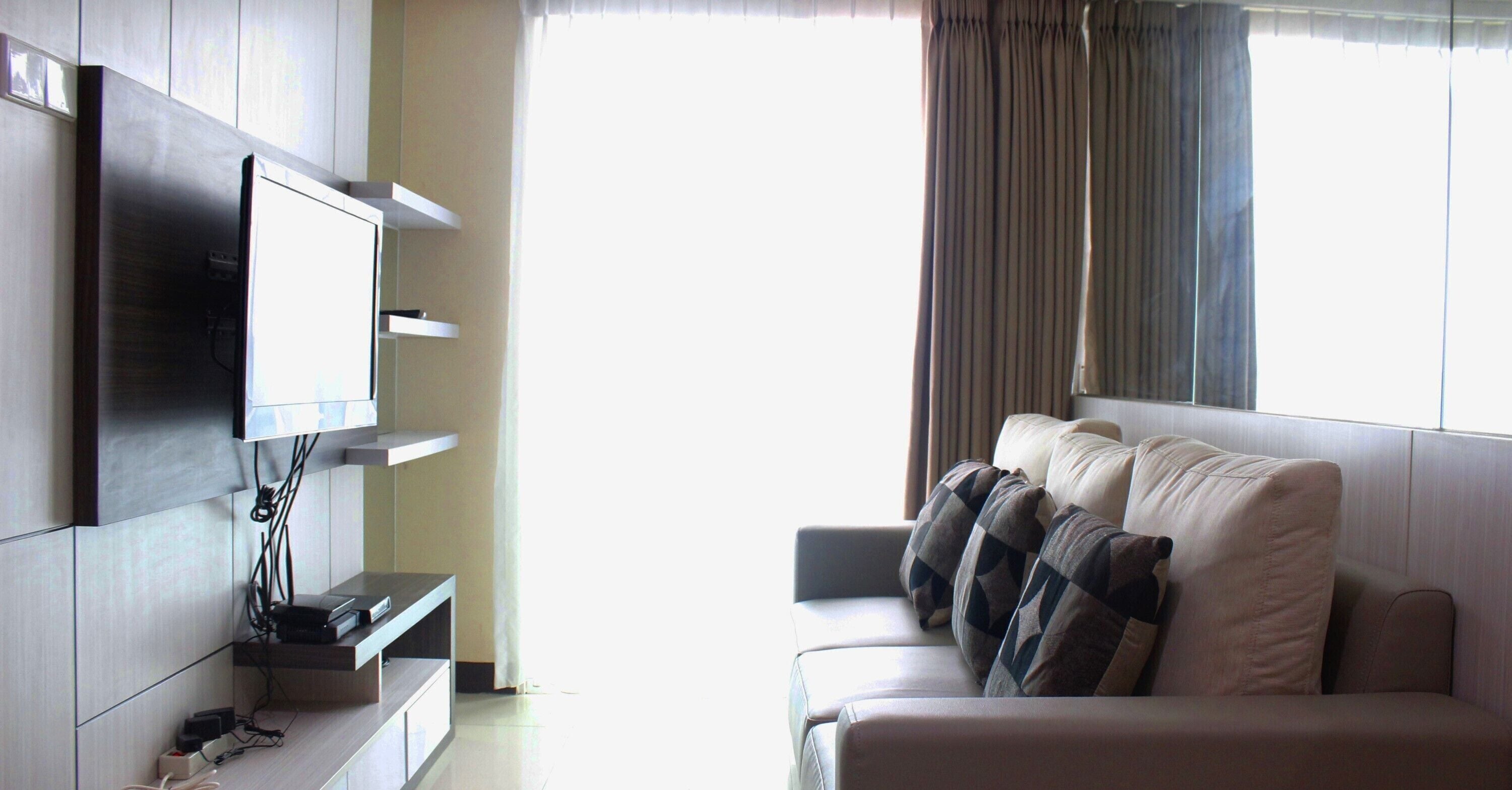 A modern living room with a flat-screen TV mounted on the wall, a sofa with patterned cushions, and a window with curtains.