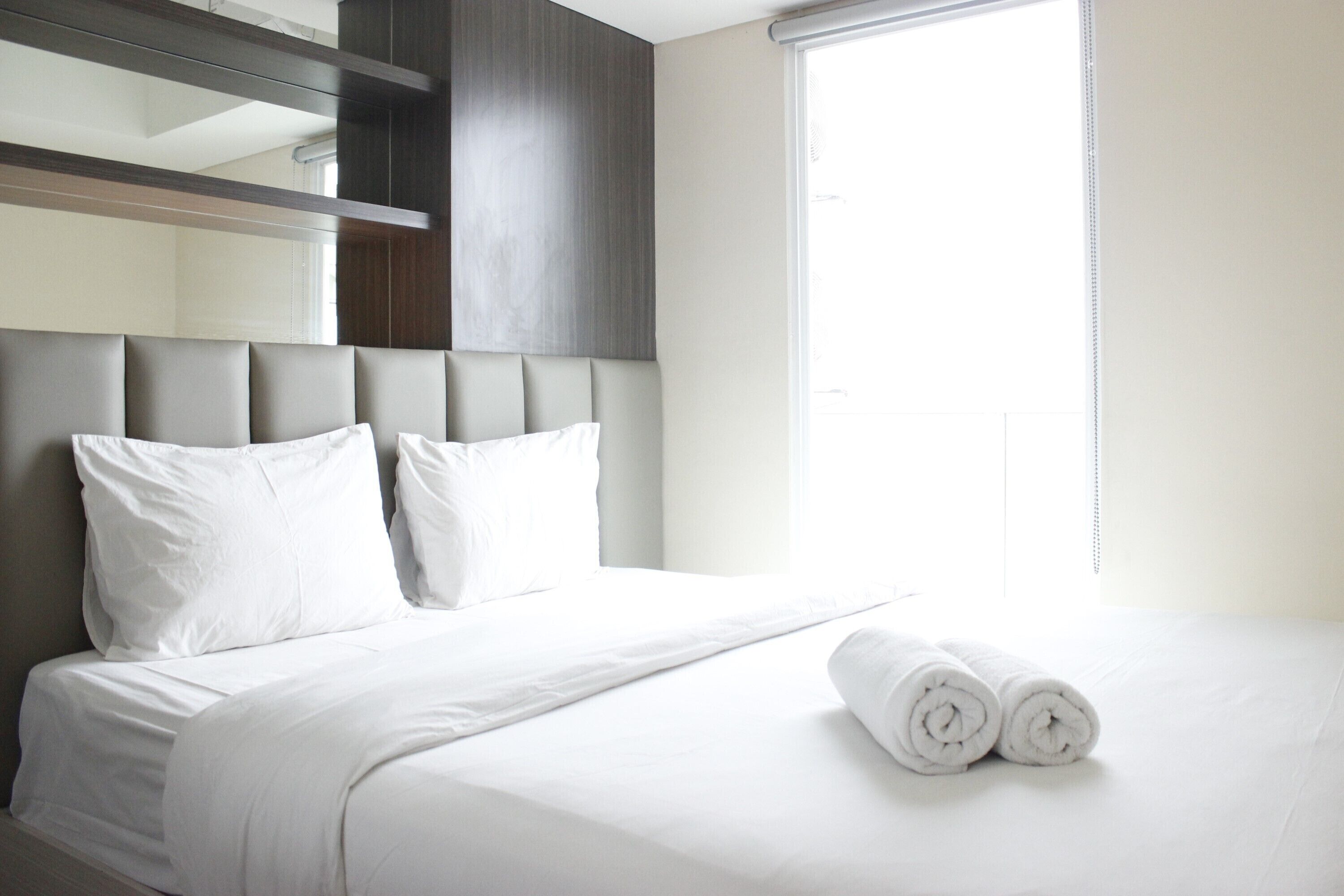 Habitación de hotel con una cama grande, ropa de cama blanca y una cama bien hecha con toallas enrolladas.