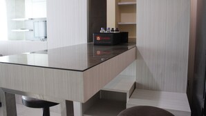 A modern kitchen with a glass countertop, a black box labeled 'travelio', and a dark-colored chair. - Brand New 2BR @ Tamansari La Grande Apartment Bandung (Bandung)