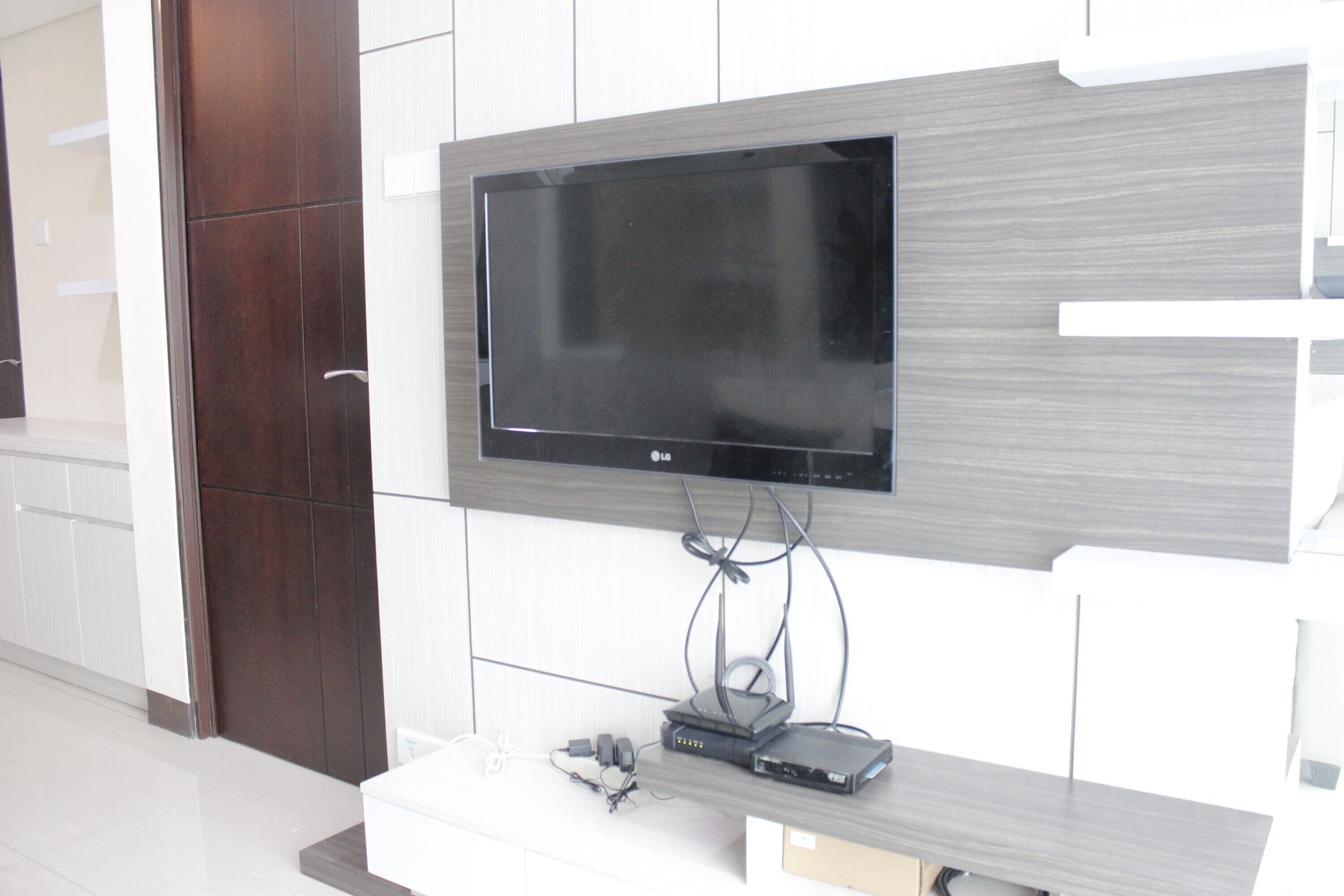 A flat-screen TV mounted on a wall with a wooden panel design, a cable management system, and a small electronic device on a white console below.