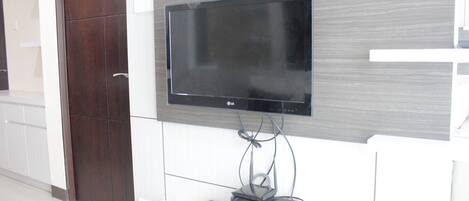 A flat-screen TV mounted on a wall with a wooden panel design, a cable management system, and a small electronic device on a white console below.