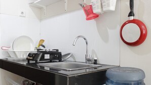 A kitchen with a black countertop, a stainless steel sink, a red pot rack, and a water dispenser. - Scenic & Trendy Studio Apartment at Gateway Pasteur (Cimahi)
