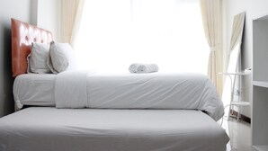 A neatly made bed with white linens and a rolled towel, a headboard, and a window with curtains. - Scenic & Trendy Studio Apartment at Gateway Pasteur (Cimahi)