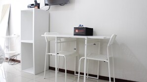 A small, clean room with a white desk, two white chairs, a black box labeled 'travelio', and a television mounted on the wall. - Scenic & Trendy Studio Apartment at Gateway Pasteur (Cimahi)