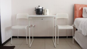 A small, clean room with a white table, two white chairs, a bed with an orange headboard, and a white kettle on the table. - Cozy & Trendy Studio at Gateway Pasteur Apartment (Cimahi)